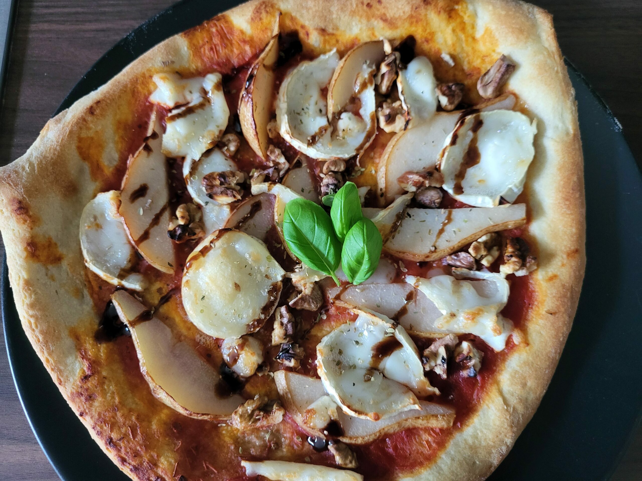 Eine eher dreieckige Pizza belegt mit Birnen, Ziegenkäse, Walnüssen und Basilikumblättern.